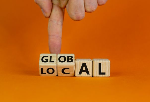  Hand turns cubes and changes the word 'local' to 'global'. Beautiful orange background. Business and local or global concept.